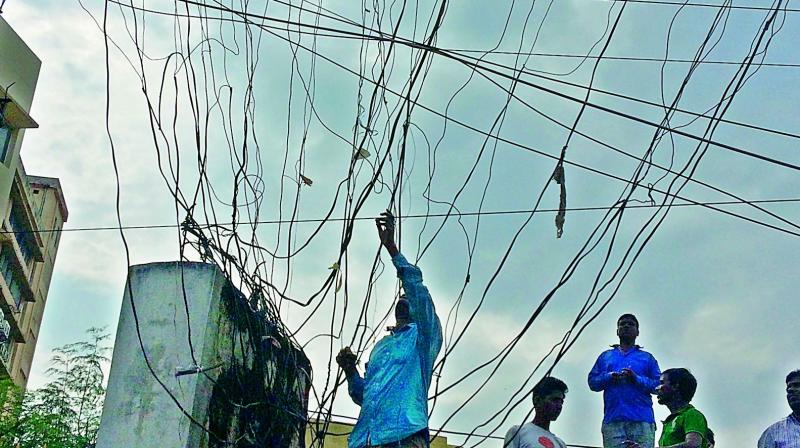 Unmindful of the danger and cocking a snook at the TS Transco, a man hooks an illegal line with a wet bamboo near Basheerbagh on Tuesday. The irony is that the activity took place next to the Lok Ayuktha office.  (Photo: P. Anil Kumar)