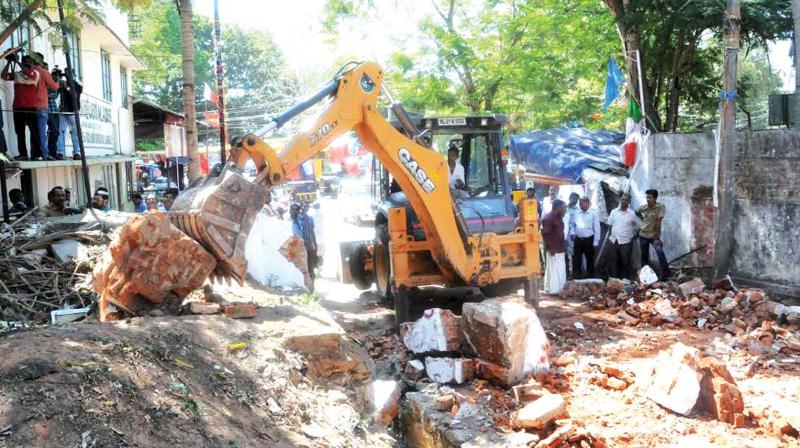 Revenue officials demolish pillars of the main entrance of the Law Academy Law College in Thiruvananthapuram on Sunday. (Photo: DC)