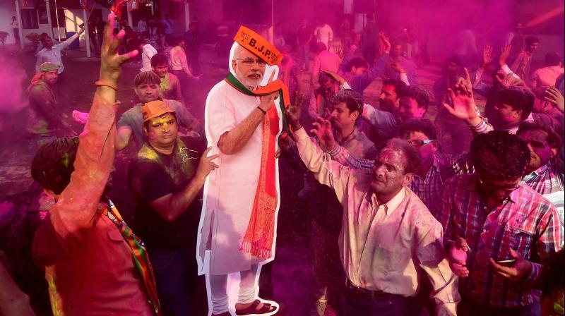 BJP workers play holi with a giant cut-out of Prime Minister Narendra Modi as they celebrate the partys victory in the UP and Uttarakhand Assembly elections, at the party headquarters in New Delhi. (Photo: PTI)