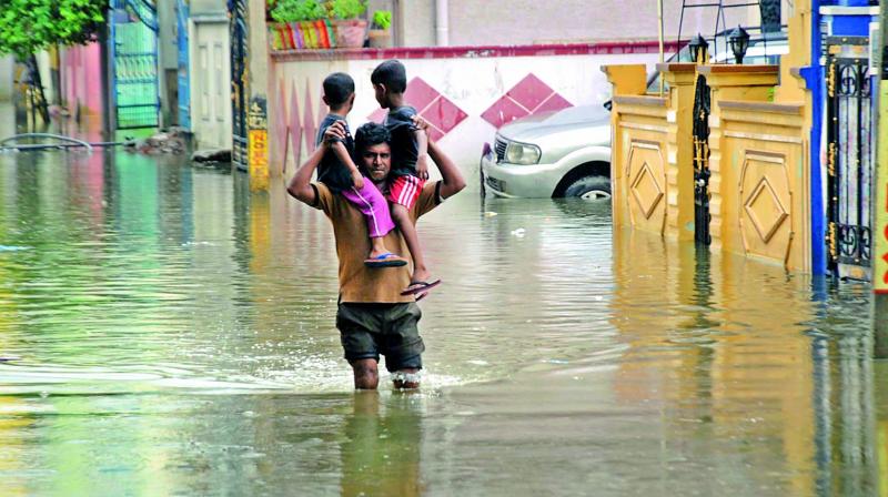 A man carries his kids on his shoulders as he tries to wade through a flooded road at Indra Nagar in Nacharam on Sunday. (Photo: DC)
