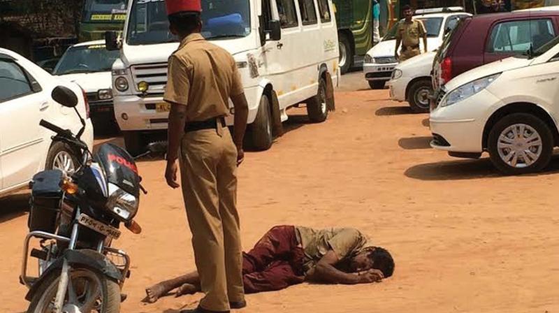 A cop in Mahe stands next to a drunkard who lost his consciousness. 	 File