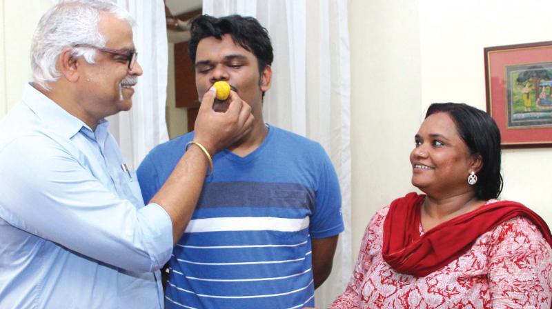 Father Prakash Kumar gives sweet to Vedanth Prakash Shenoy, who secured second rank in state engineering entrance examination, in Kottayam on Tuesday. Vedanths mother Capt. Sheena Ravi looks on. (Photo: Rajeev Prasad)