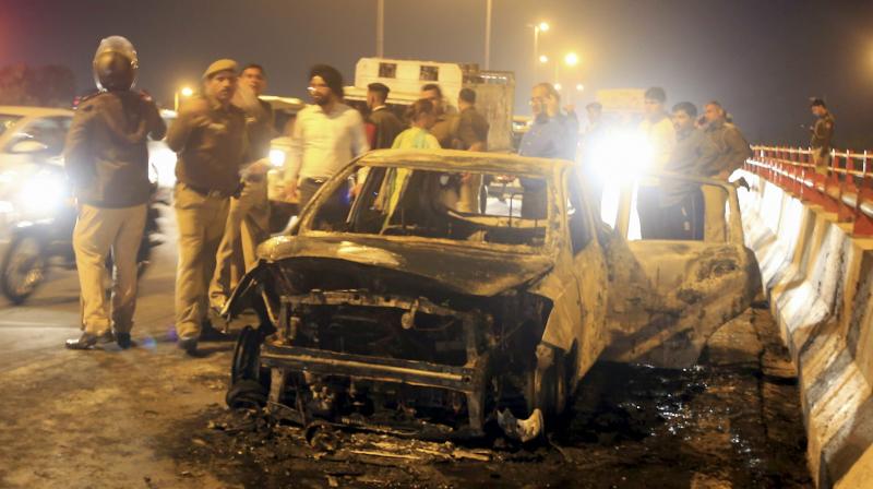 Police and people stand near a charred car which caught fire near Akshardham in New Delhi. (Photo: PTI)