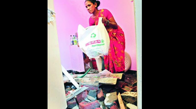 A woman at Devarakonda Basti clears the debris inside her home which was damaged by rain. (Photo: DC)