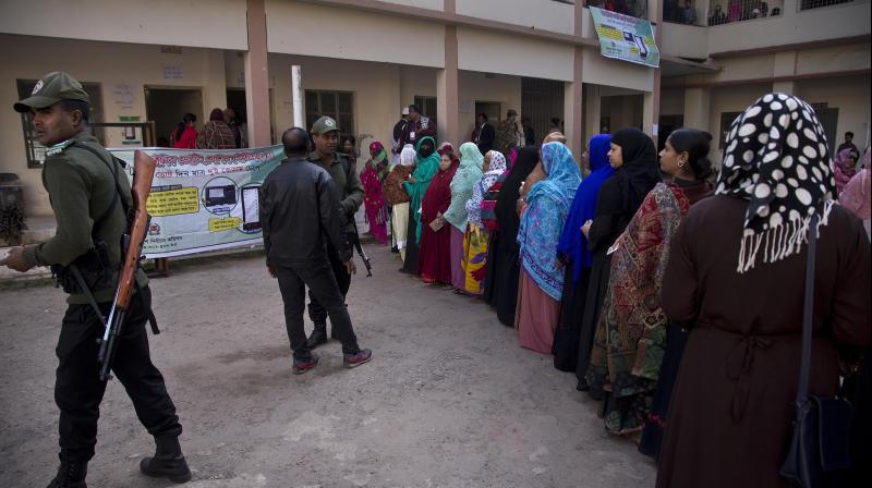 Bangladeshi security personnel stand guard as women line up to cast their votes outside a polling station in Dhaka on Dec 30. (Photo: AP)