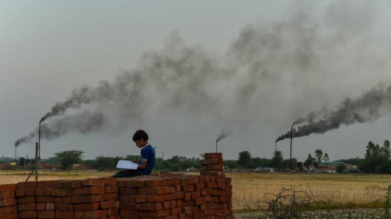 A child reads from a book, as thick black smoke rises in the sky from the glue factories at Dakari village of Unnao district near Kanpur. (Photo: PTI)