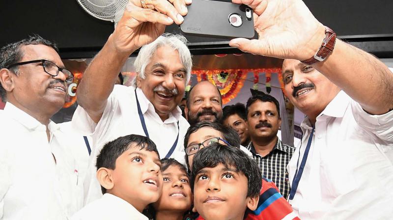 Former chief minister Oommen Chandy and M.K. Raghavan, MP, take a selfie with children gathered at the clinic. 	DC