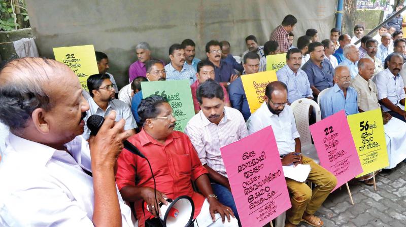 Members of contractors association stage sit-in protest in front of corporation office on Thursday.