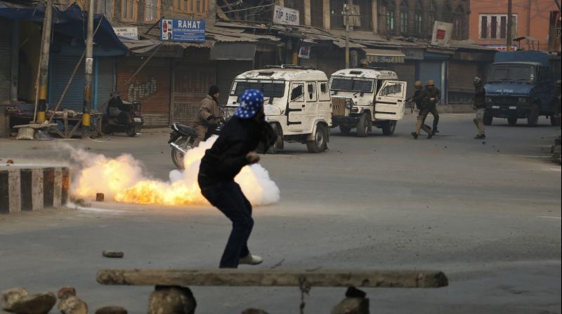 A civilian crosses a road as a tear gas shell directed towards protestors explodes near him in Srinagar. (Photo: AP)