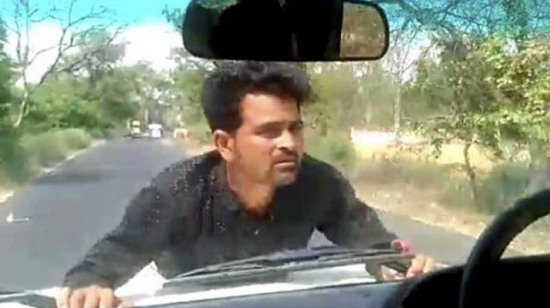 A man clings on to the bonnet of a car in UPs Ramnagar as a block development officer drives for 4 km. (YouTube | Screengrab)