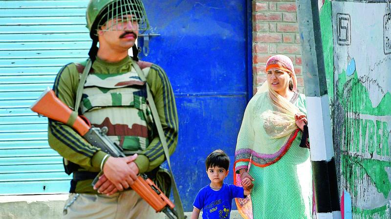 A woman and her son look on as a security guard stands at a block road during curfew imposed on the first death anniversary of Hizbul Mujahideen commander Burhan Wani, in Srinagar, on Saturday. (Photo: PTI)