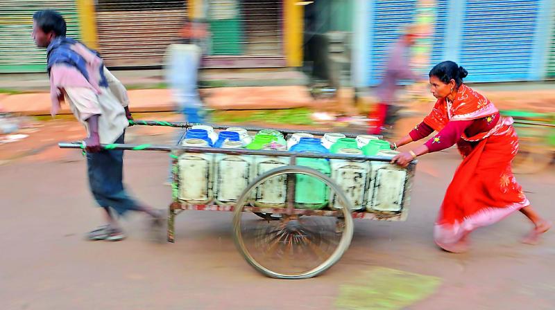 Labourers carry tins of drinking water for distribution to food stalls in Agartala on Tuesday. (Photo: AFP)