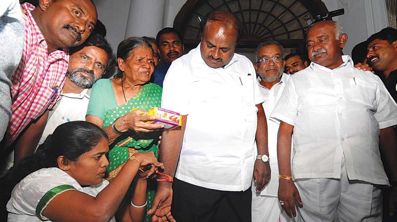 A woman ties a rakhi on CM H.D. Kumaraswamys wrist as the state JD(S) chief A.H. Vishwanath looks on in Mysuru on Tuesday 	(Photo: KPN)