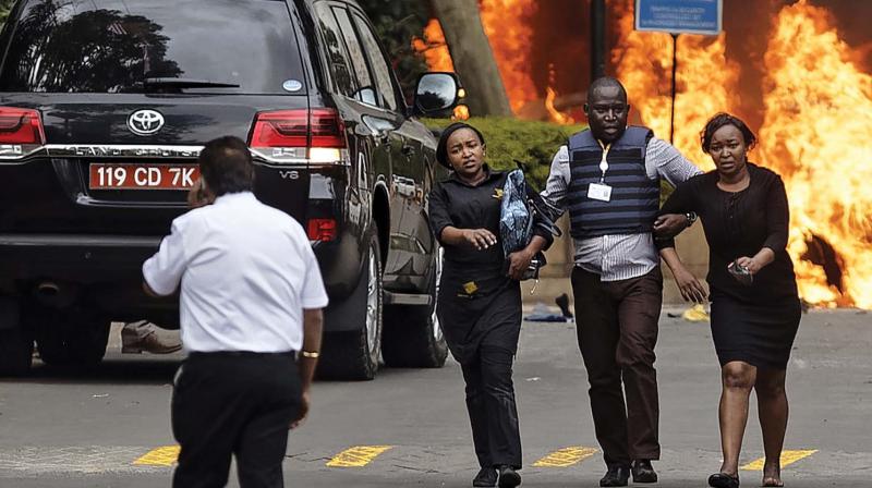 Security forces help civilians flee the scene as cars burn behind, at a hotel complex in Nairobi on Tuesday