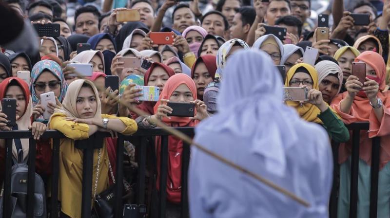 People use their mobile phones to take pictures as a Sharia law official whips a woman who is convicted of prostitution during a public caning outside a mosque in Banda Aceh. (Photo: AP)