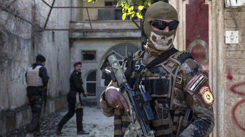 A masked Iraqi security officer stands guard outside a house during a raid on suspected Islamic State group fighters. (Photo: AP)
