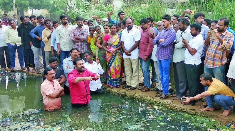 Nellore rural MLA K. Sridhar Reddy enters sewage water in protest against the official negligence in constructing a protection wall for the walkway bridge over the drainage at Chanakya puri colony in Nellore city on Wednesday.  (DC)