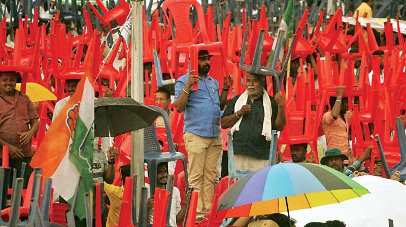 Supporters of JD(S) and Congress use chairs to protect themselves from rain during the swearing-in ceremony in Bengaluru on Wednesday.  (Photo:DC)