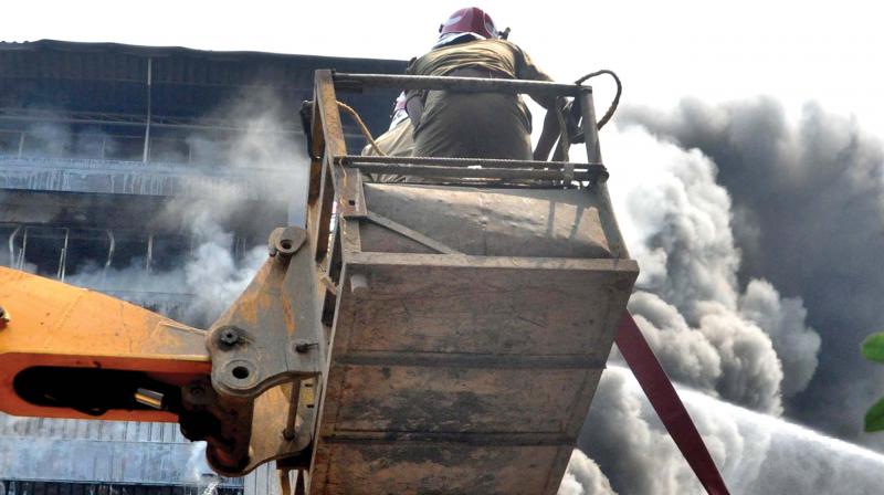 Firefighters engaged in dousing flames using a JCB following the inferno at a footwear godown-cum-office building in Kochi on Wednesday.