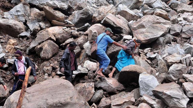 People trek through the boulders that landed near the bridge in the landslide at Kuderachola in Nelliyampathy. (Photo: DC)