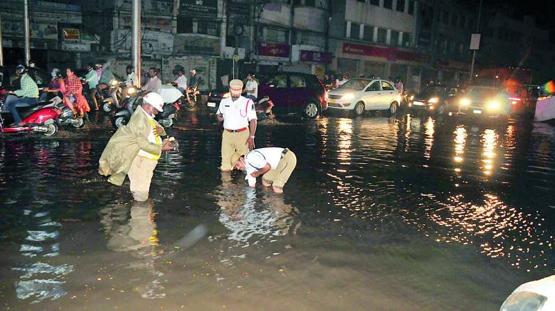 Traffic cops clear obstruction from road flooded with rain water after heavy rains battered the city on Friday night.  (Photo: DECCAN CHRONICLE)