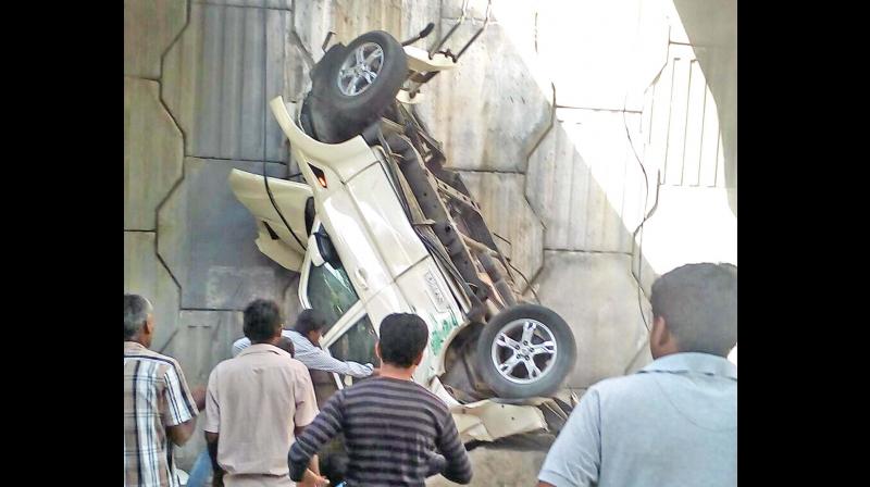 Onlookers gather around the car that fell off from a flyover near Avinashi in Tirupur district on Friday. (Photo: DC)