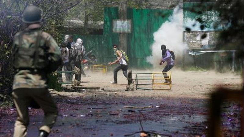 Kashmiri students throw stones on Indian policemen as tear smoke shell explodes near them. (Photo: PTI)