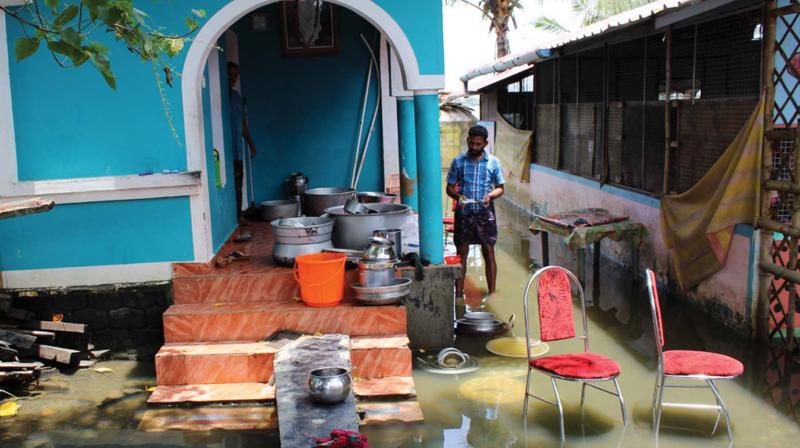 A restaurant owner from Kuppuram whose shop has been submerged rinses utensils in floodwater.