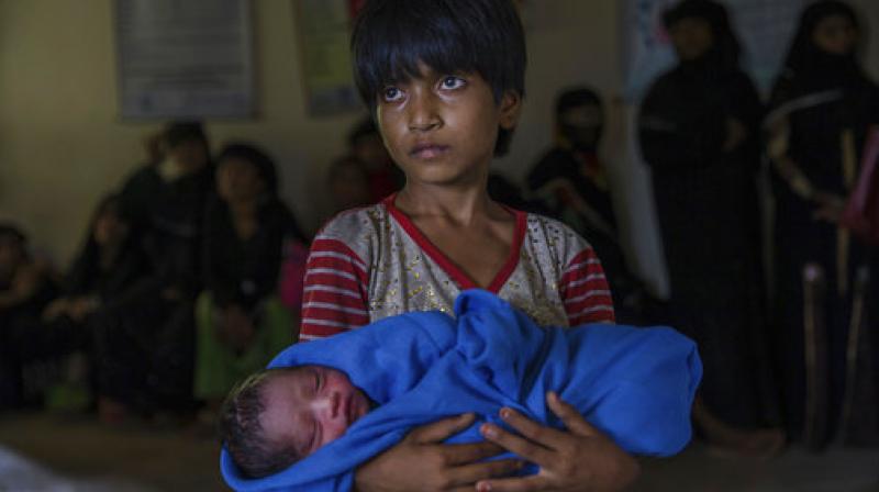 Rohingya Muslim girl Afeefa Bebi, who recently crossed over from Myanmar into Bangladesh, holds her few-hours-old brother as doctors check her mother Yasmeen Ara at a community hospital in Kutupalong refugee camp. (Photo: PTI)