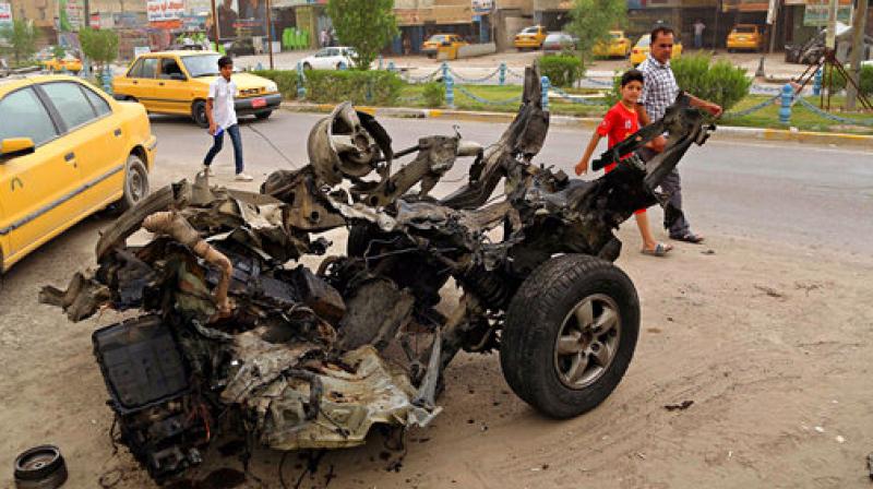 Civilians pass a destroyed car in the a car bomb explosion in southwestern Baghdad, Iraq. (Photo: AP)