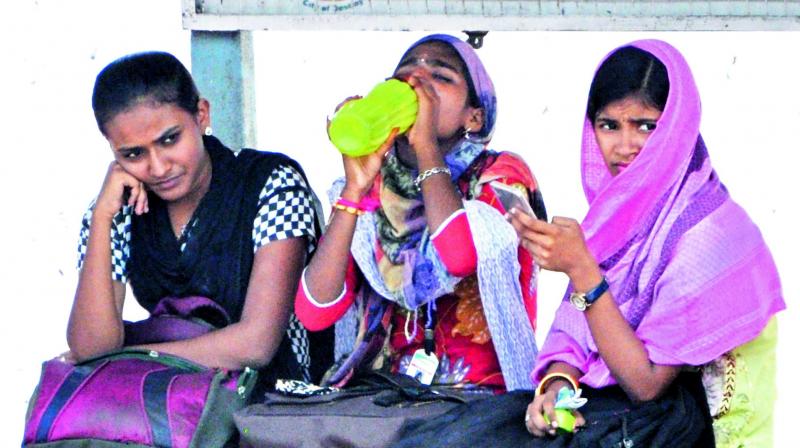 Youngsters cover their faces with cloth to beat the soaring heat at a bus stop in Visakhapatnam on Thursday. (Photo: DC)