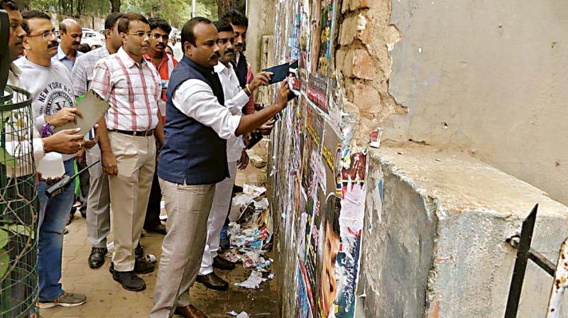 Mayor Sampath Raj tears off posters from a wall as part of the two-day drive to remove flexes, banners and posters across the city, in Bengaluru on Saturday 	DC