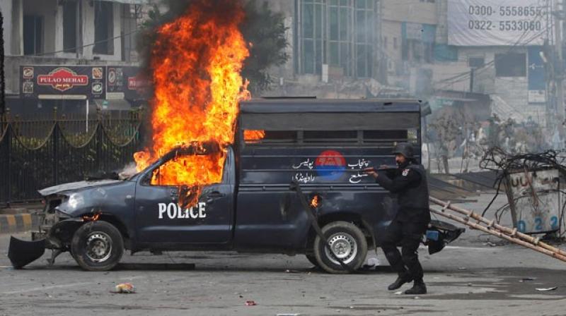 A Pakistani police officer aims his gun towards the protesters next to a burning police vehicle during a clash in Islamabad, Pakistan. (Photo: AP)