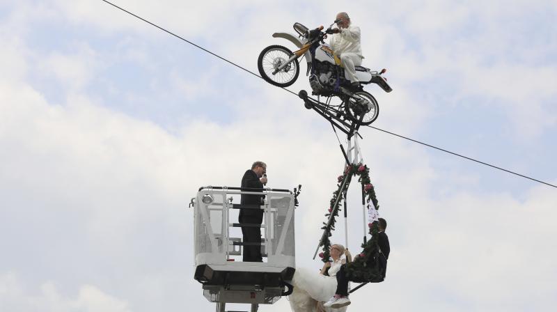 Pastor Stefan Gierung, left, stands in a cage atop of a fire service ladder in front of bride Nicole Backhaus, center, and groom Jens Knorr, right, both sitting in a swing dangling under a motorcycle with artist Falko Traber, top, during the wedding ceremony atop a tightrope in Stassfurt, Germany, Saturday, June 16, 2018. (Photo: AP)