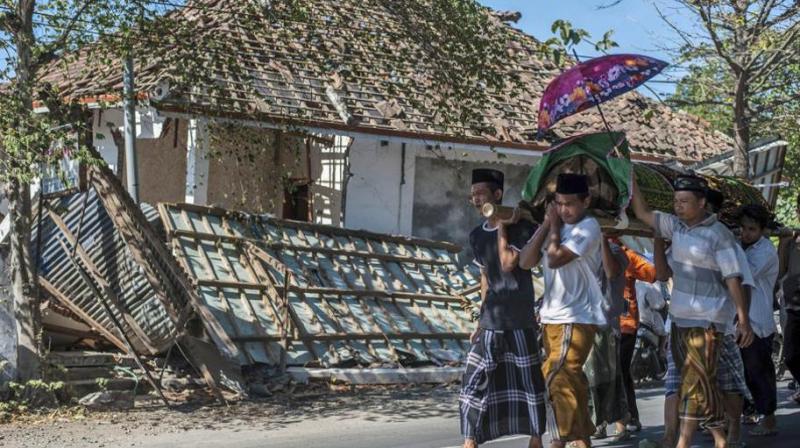Indonesian men carry the body of a victim of last weeks earthquake past a damaged building during a funeral in Gangga, Lombok Island, Indonesia on August 12.(Photo: AP)