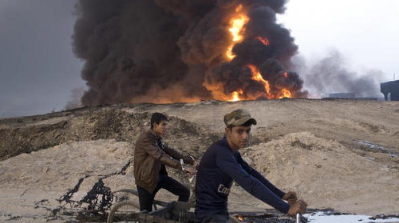 Youths ride bicycles next to a burning oil well in Qayara, about 31 miles (50 km) south of Mosul, Iraq. (Photo: AP)