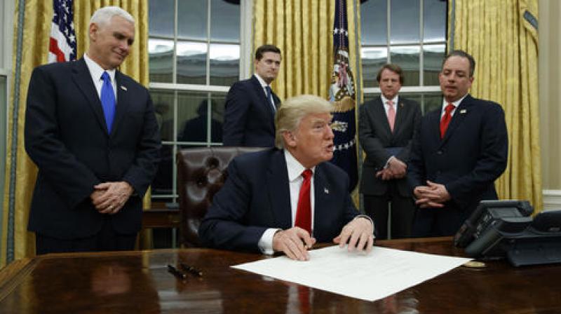 Vice President Mike Pence watches at left as President Donald Trump prepares to sign his first executive order, Friday, Jan. 20, 2017, in the Oval Office of the White House in Washington.