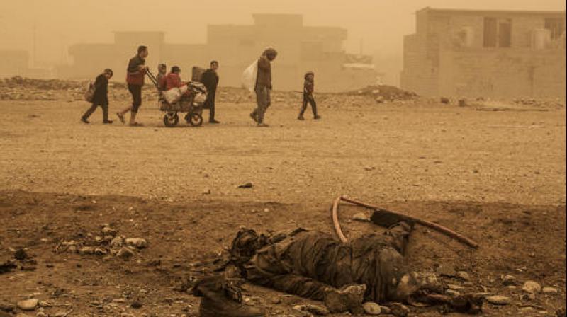 A group of civilians pass close to the body of an Islamic State militant. (Photo: )