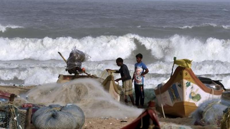 Fishermen stand near boats as waves break on the cost of the Bay of Bengal in Chennai on Thursday. (Photo: PTI)
