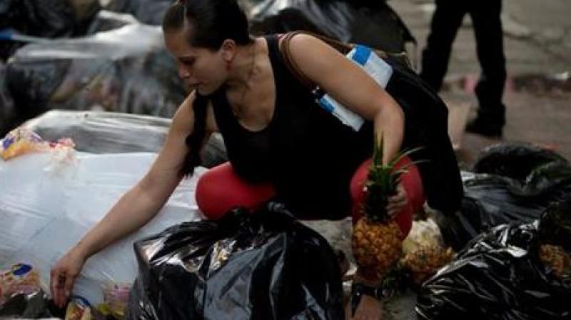 A pregnant woman who did not want to be named, holding a pineapple in one hand as she continues to pick through garbage bags outside a supermarket in downtown Caracas, Venezuela. (Photo: AP)