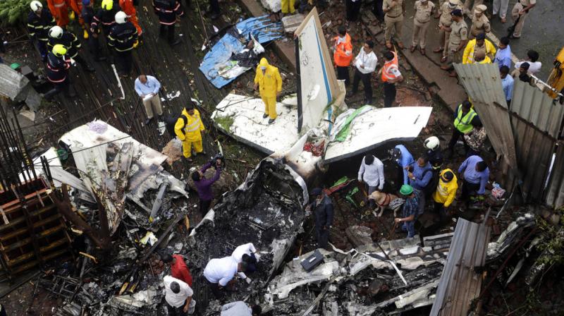 Rescuers stand amid the wreckage of a private chartered plane that crashed in Ghatkopar area, Mumbai. The plane hit an open area at a construction site for a multistory building in a crowded area with many residential apartments. 5 people including one on the ground were killed. (Photo: AP)