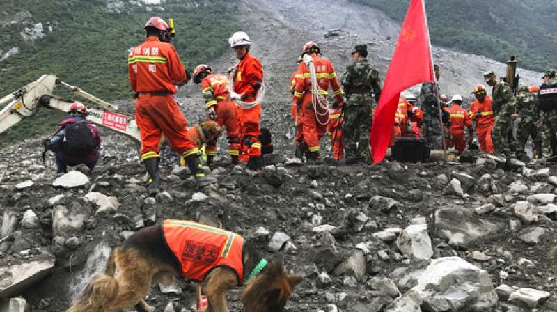 Rescuers with sniffer dogs stand near earth moving equipment digging at the site of a landslide in Xinmo village in Maoxian County in southwestern Chinas Sichuan Province. Crews searching through the rubble left by a landslide that buried a mountain village under tons of soil and rocks in southwestern China found bodies, but many others remained missing. (Photo: AP)
