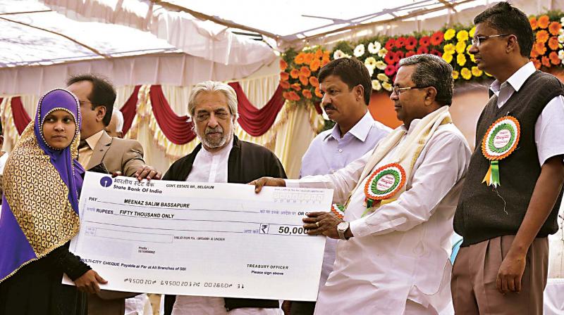 Chief Minister Siddaramaiah hands over a cheque to a beneficiary of a welfare scheme at Yamakamaradi in Belagavi district on Friday. (Photo: KPN)