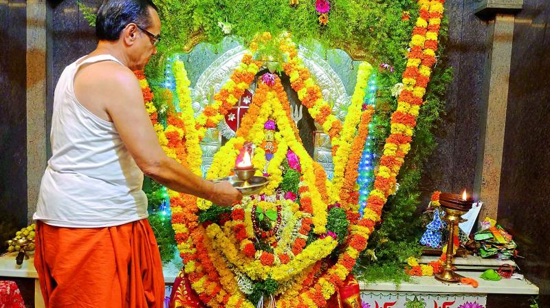The temple priest performs rituals to the idol almost fully covered by floral decorations. (Photo: P. Surendra)