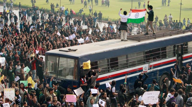 Protesters, atop a police bus, hold national flag during a demonstration at Vijay Chowk in New Delhi. (Photo: PTI/File)