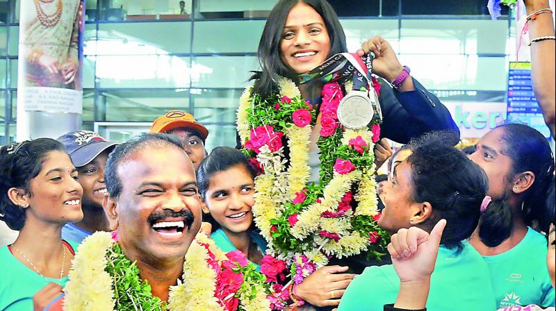 Asian Games double silver medallist Dutee Chand is jubilant as she is hoisted upon her arrival at the Hyderabad airport on Saturday. Her coach N. Ramesh (garlanded, front left) is understandably excited. (Photo: Deepak deshpande)