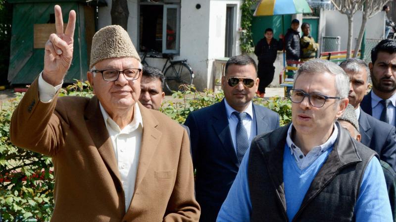 Former Union Minister and Congress-National Conference joint candidate Farooq Abdullah shows victory sign as his son and former Chief Minister Omar Abdullah looks on outside a polling station during voting for Srinagar parliamentary seat. (Photo: PTI)