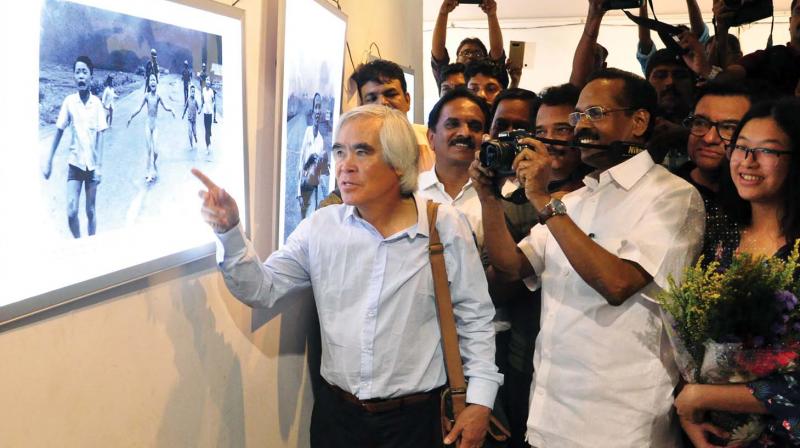 Nick Ut points at his photograph of a Vietnamese girl running aflame during the Vietnam war, while minister T.P. Ramakrishnan attempts a click during the opening ceremony of Nick Ut photo exhibition at Art Gallery, Kozhikode on Saturday.	(Photo: Venugopal)