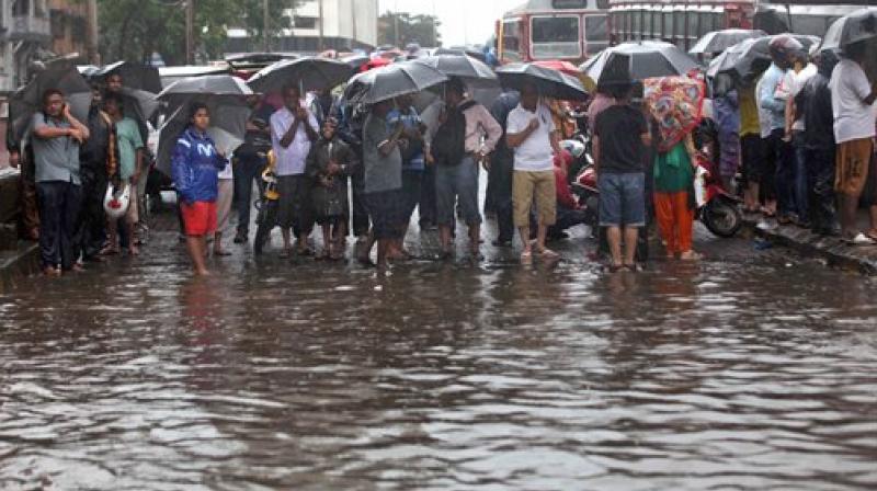 People stand stranded during heavy rain at a waterlogged street near Dadar in Mumbai on Tuesday. (Photo: PTI)