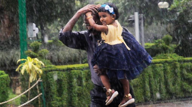 A man with child in his arm runs for cover after being caught in a sudden spell of rain at Museum in Thiruvananthapuram on Saturday.  (Photo: A.V. MUZAFAR)